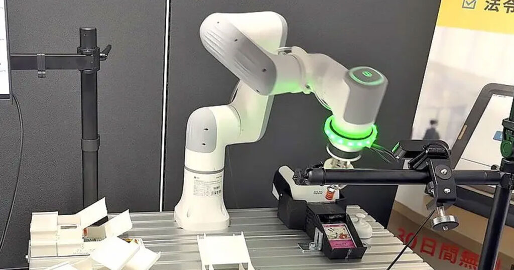 株式会社コモンプロダクツの展示会ボで稼働テストを行うトレカ自動仕分けAIロボットアーム。カメラモジュールと吸着パッドを備えたアームが、トレイ上のカードを精密に識別・搬送している研究開発の様子。
