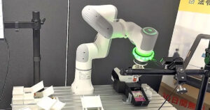 株式会社コモンプロダクツの展示会ボで稼働テストを行うトレカ自動仕分けAIロボットアーム。カメラモジュールと吸着パッドを備えたアームが、トレイ上のカードを精密に識別・搬送している研究開発の様子。